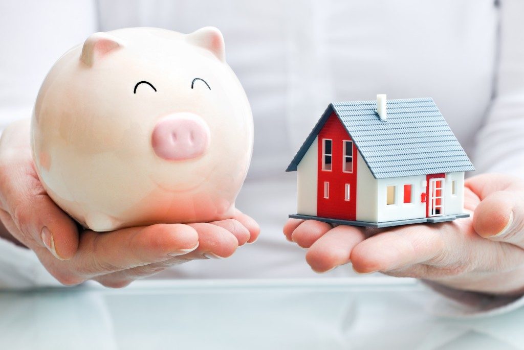 Hands holding a piggy bank and a house model