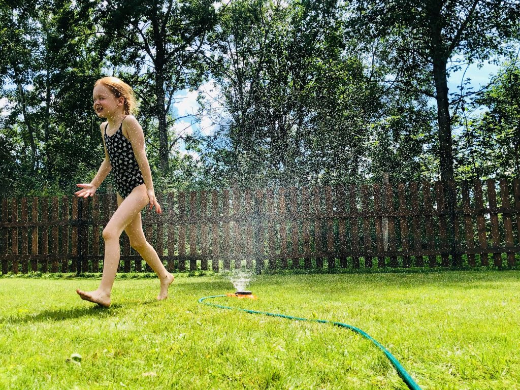 kid playing with sprinkler in backyard