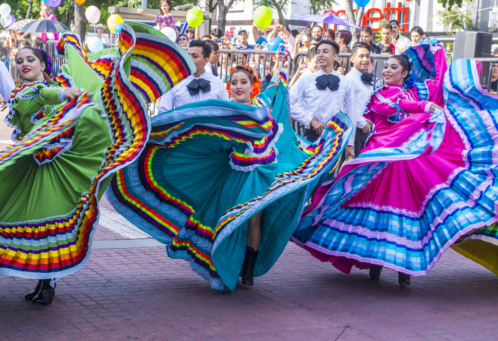 Ladies dancing while wearing colorful clothes on the street.
