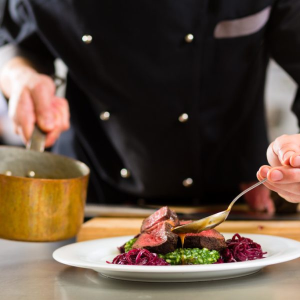A chef plating a beef dish in the kitchen