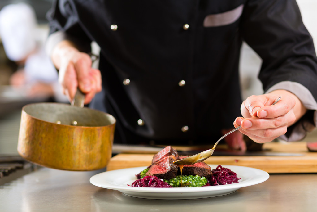 A chef plating a beef dish in the kitchen